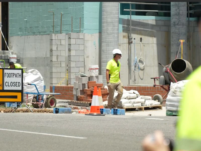 Construction worker at active roadwork site with traffic management cones and building materials