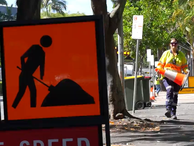 Roadwork warning sign with traffic control worker carrying safety cone on urban roadside