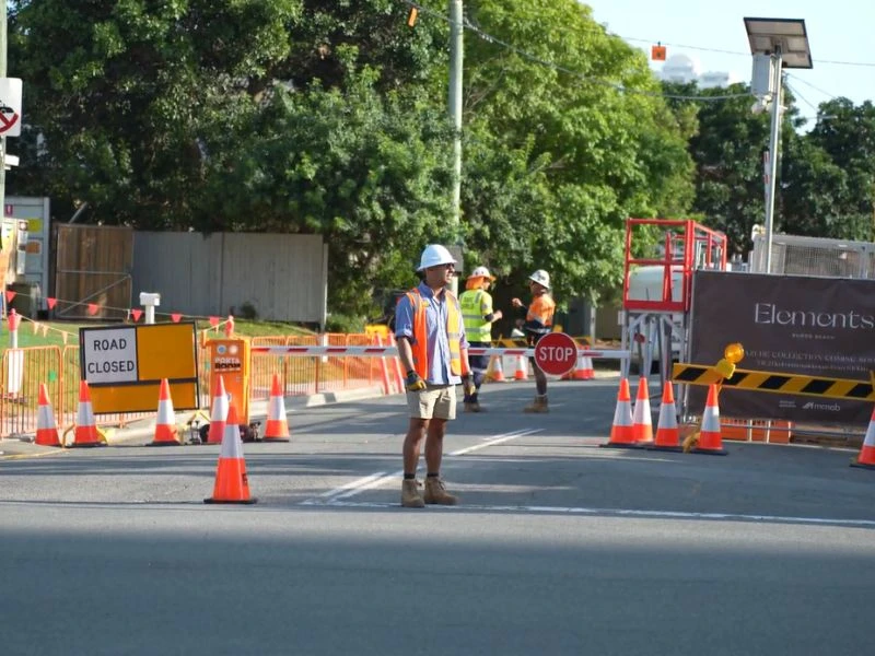 Traffic control workers managing road closure with safety cones and stop signage on urban street